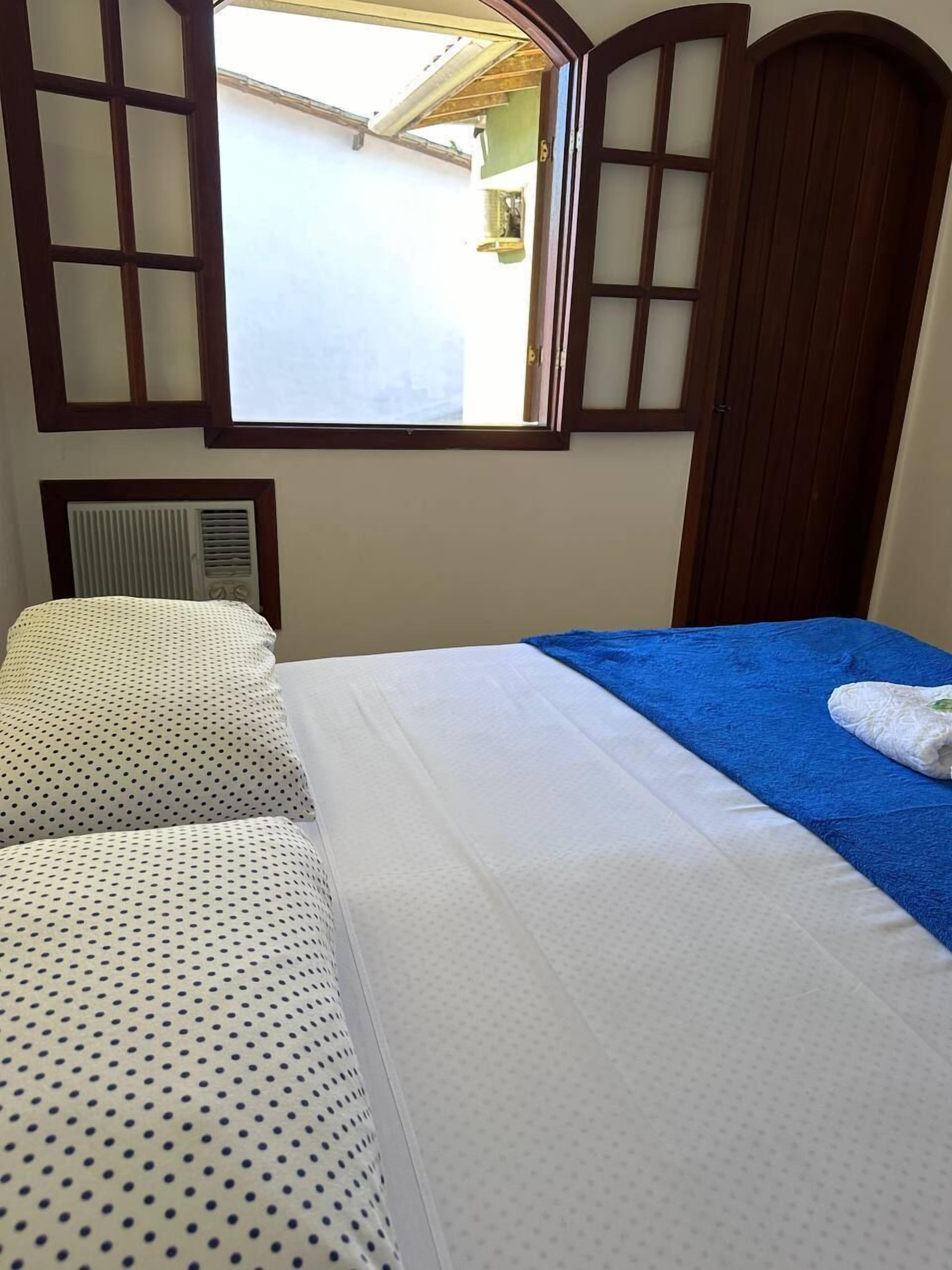 Un dormitorio con cama, dos almohadas, una ventana y un armario de madera.