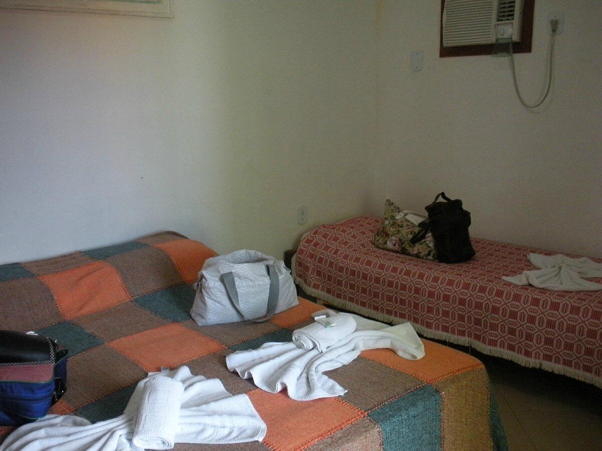 Une petite pièce simple, avec un lit simple, un canapé et une petite table. Un sac est posé sur le canapé et une valise sur le sol.