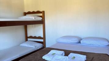 A single bed with a brown blanket and two folded towels, a lower bunk bed, and two pillows on a white mattress.