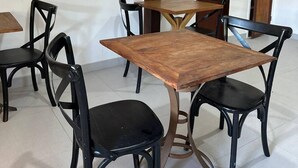 A dining area with a wooden table and black chairs, a decorative wall with floral artwork, and a wooden door in the background. - Pousada Encanto Torrely (Búzios)