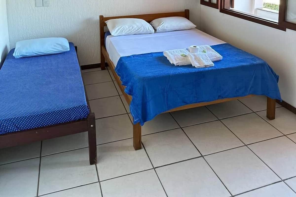 Une chambre avec deux lits simples, l’un recouvert d’une couvre-lit à pois bleus et l’autre d’une couvre-lit bleue, un plafond en bois et une fenêtre donnant sur un paysage verdoyant.