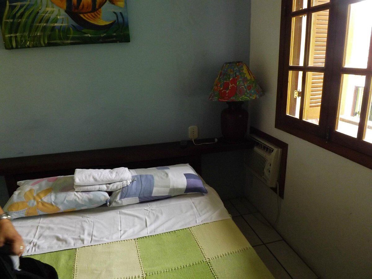 Quarto de hotel com cama, radiador, janela com persianas e um quadro na parede.