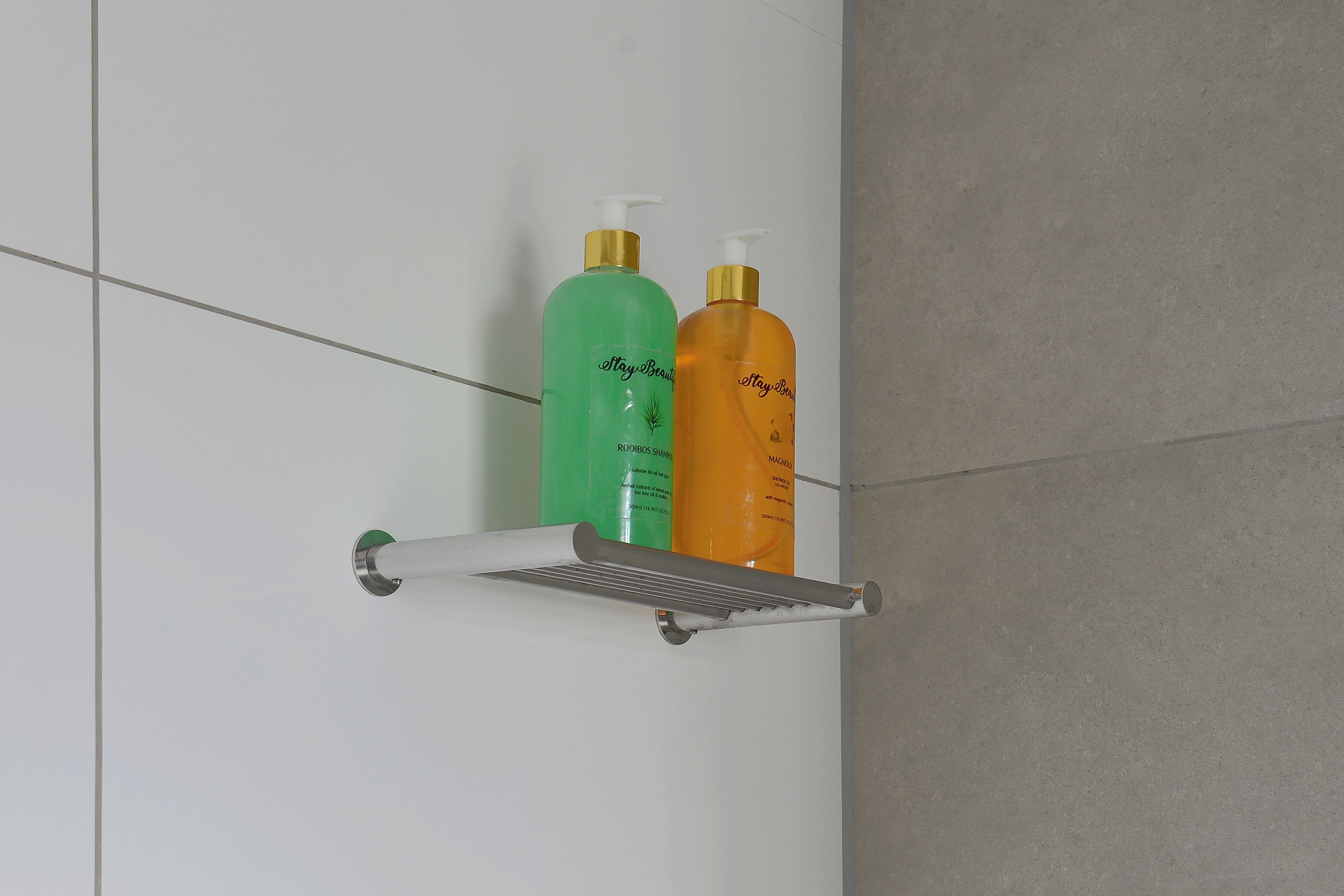 A bathroom with a white wall and a metal shelf holding two bottles of shampoo.