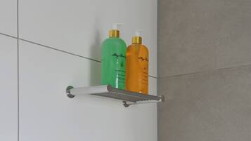 A bathroom with a white wall and a metal shelf holding two bottles of shampoo.