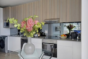 Une cuisine moderne avec une table en verre, un vase rempli de fleurs et un panier de fruits.
