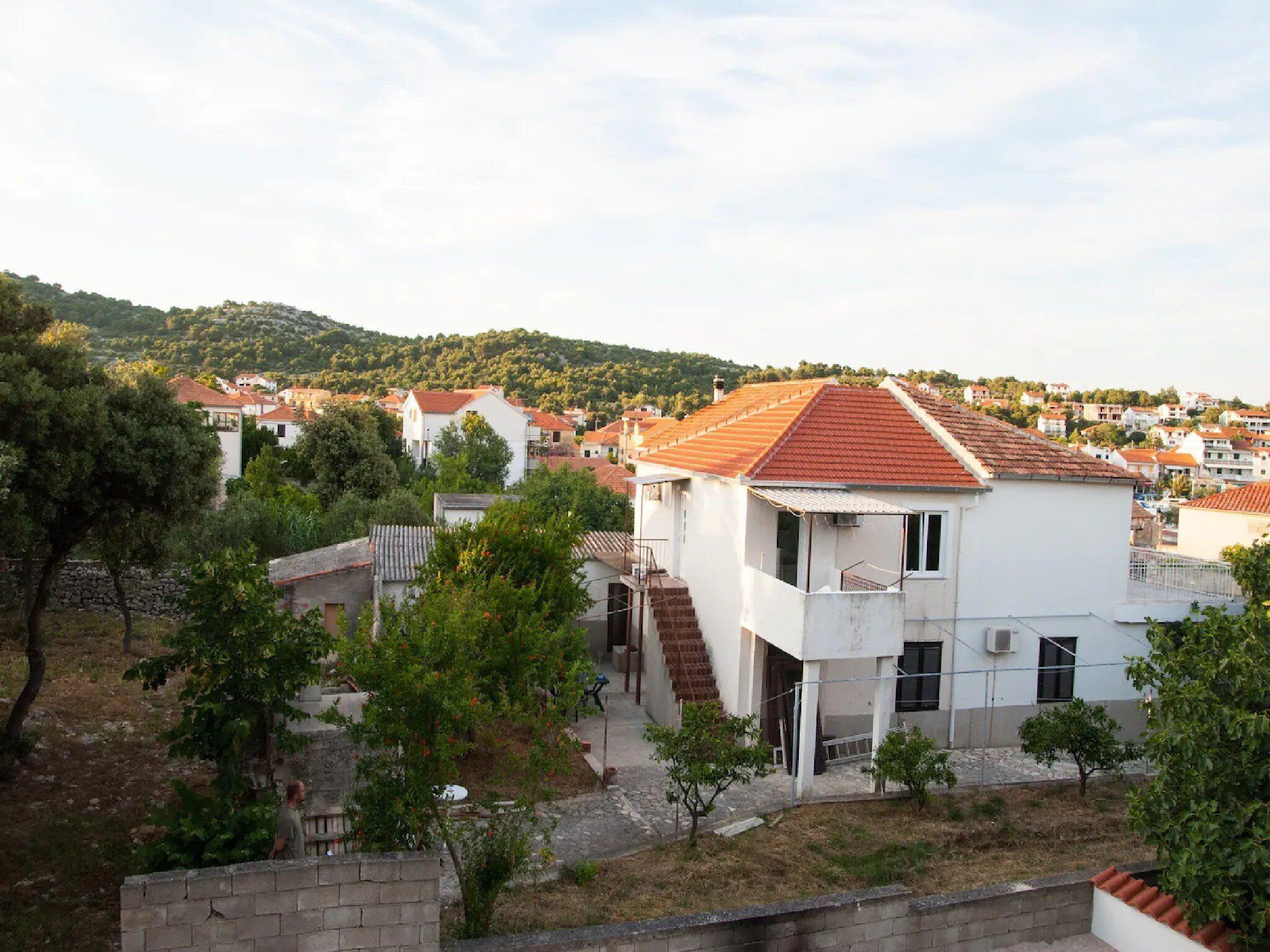 Zona residencial con casas de paredes blancas y techos de tejas rojas, rodeada de vegetación y un paisaje montañoso.