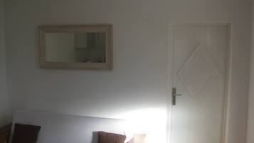 Una habitación con una cama blanca, una almohada marrón, un espejo en la pared y una puerta con un diseño en forma de rombo.