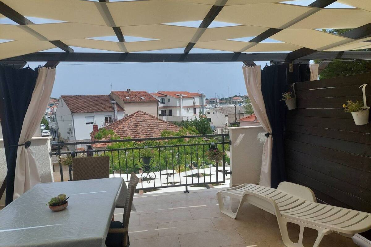A covered outdoor seating area with a table and chairs, a view of buildings in the background, and a railing.
