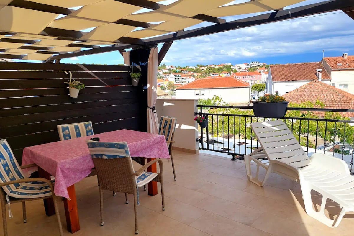 A covered outdoor seating area with tables and chairs, a view of the cityscape, and a balcony with a railing.