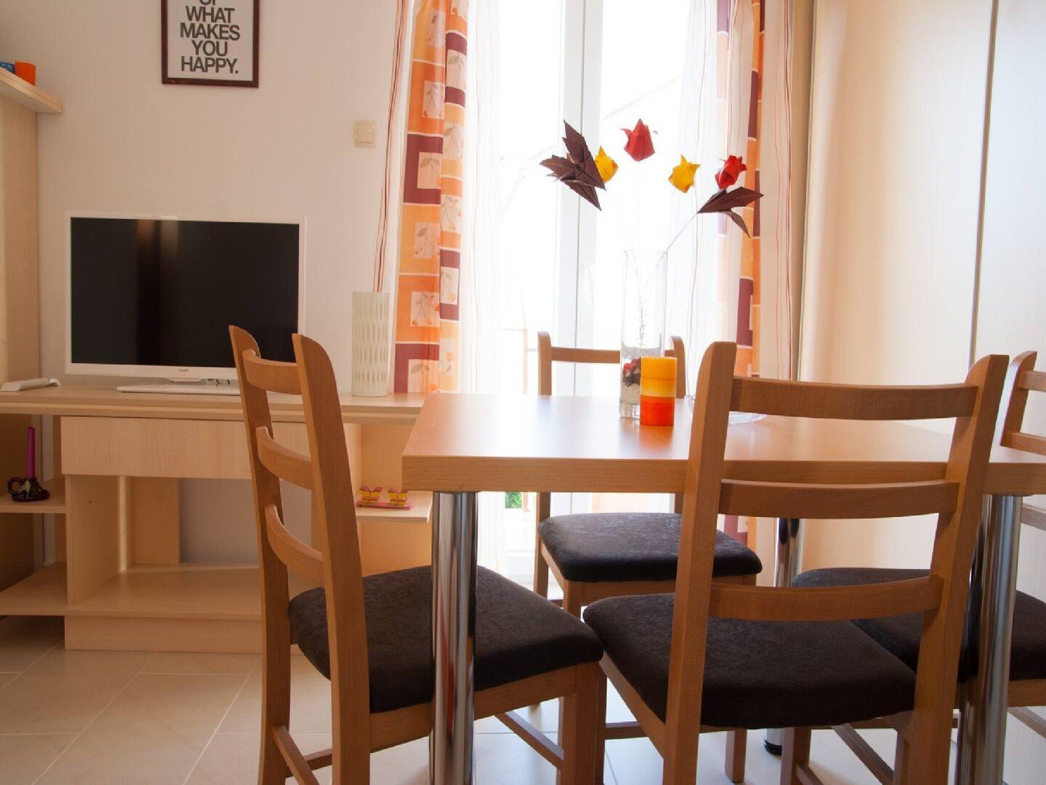 Een eethoek met een houten tafel en stoelen, een televisie op een bureau en een raam met gordijnen.