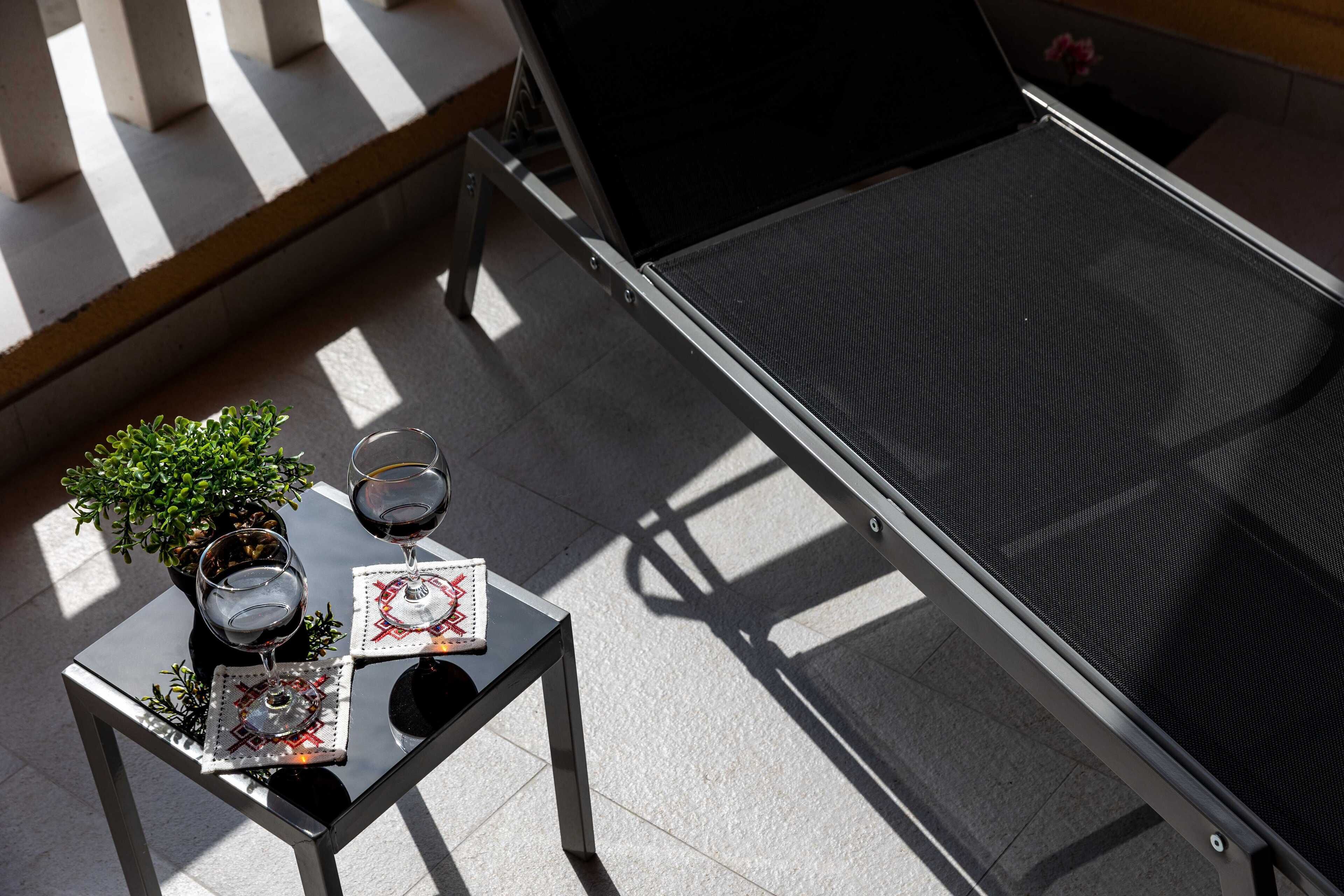 Un espace extérieur ensoleillé, aménagé avec des sièges, où une table est dressée pour deux personnes, agrémentée d’une petite plante en pot et de deux verres à vin.