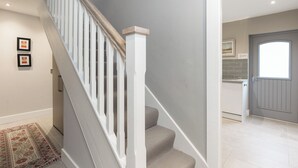 Una escalera con barandillas blancas y alfombra color crema que lleva a una zona de cocina con una puerta gris y una ventana.
