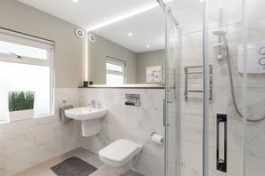 Een moderne badkamer met een douchecabine van glas, een wit wastafelmeubel en een toilet.