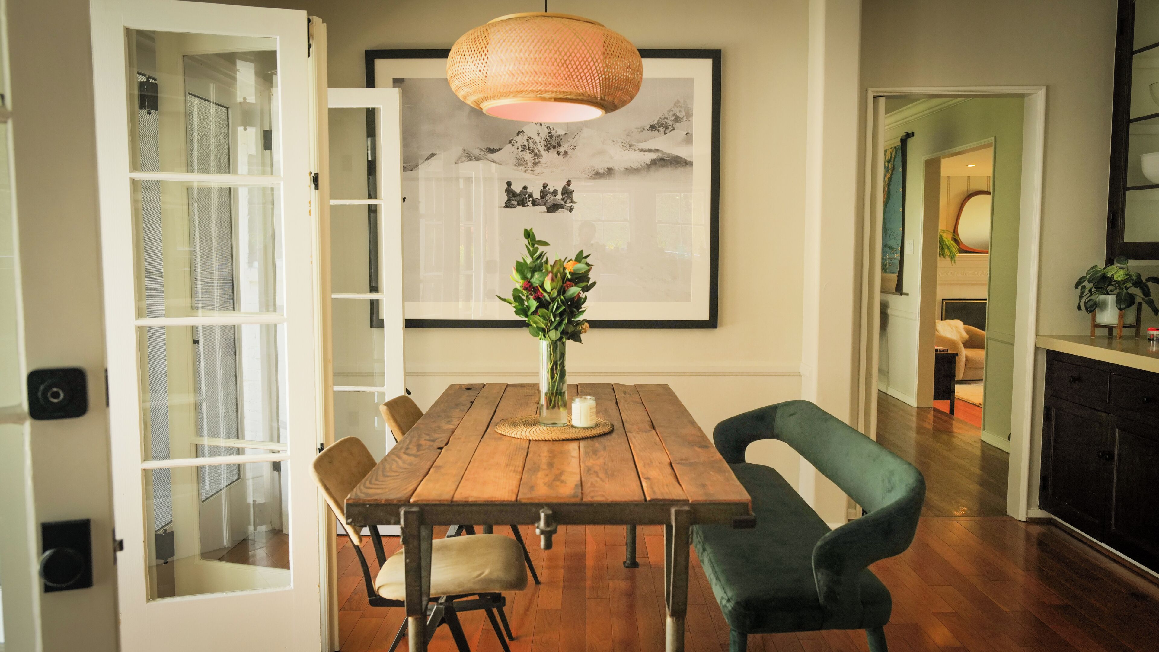 A dining area with a wooden table, chairs, a vase with flowers, and a framed picture on the wall.