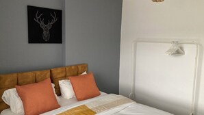 A neatly made bed with a brown headboard, white and orange pillows, and a gold and white striped blanket. A black artwork with a deer head is on the wall. - Cozy and Central City Apartment in Liverpool (Liverpool)