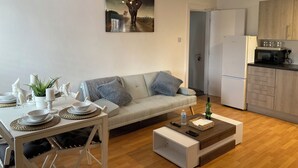 A modern living room with a sofa, coffee table, and dining table set for a meal. A kitchen with a microwave and cabinets is visible in the background. - Cozy and Central City Apartment in Liverpool (Liverpool)
