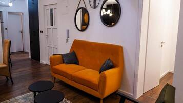 Una sala de estar con sofá, dos mesitas auxiliares, un tapete estampado y una puerta.