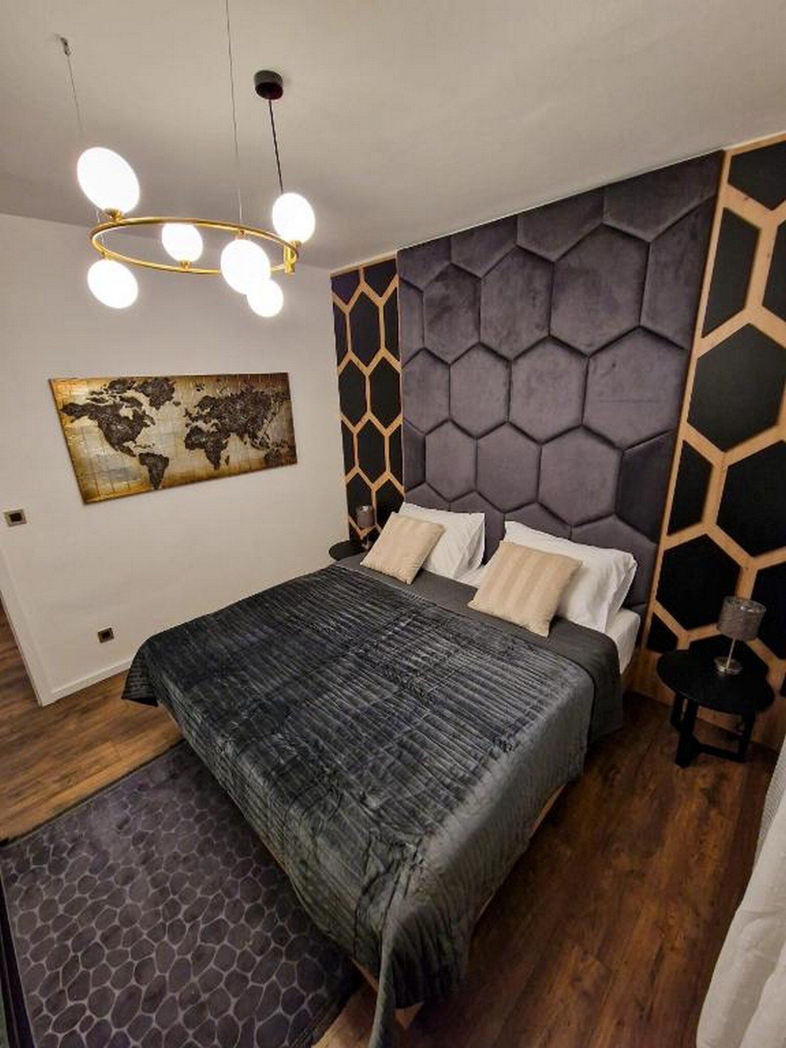 A modern bedroom with a geometric-patterned headboard, a world map artwork, and a bed with a dark textured bedspread.