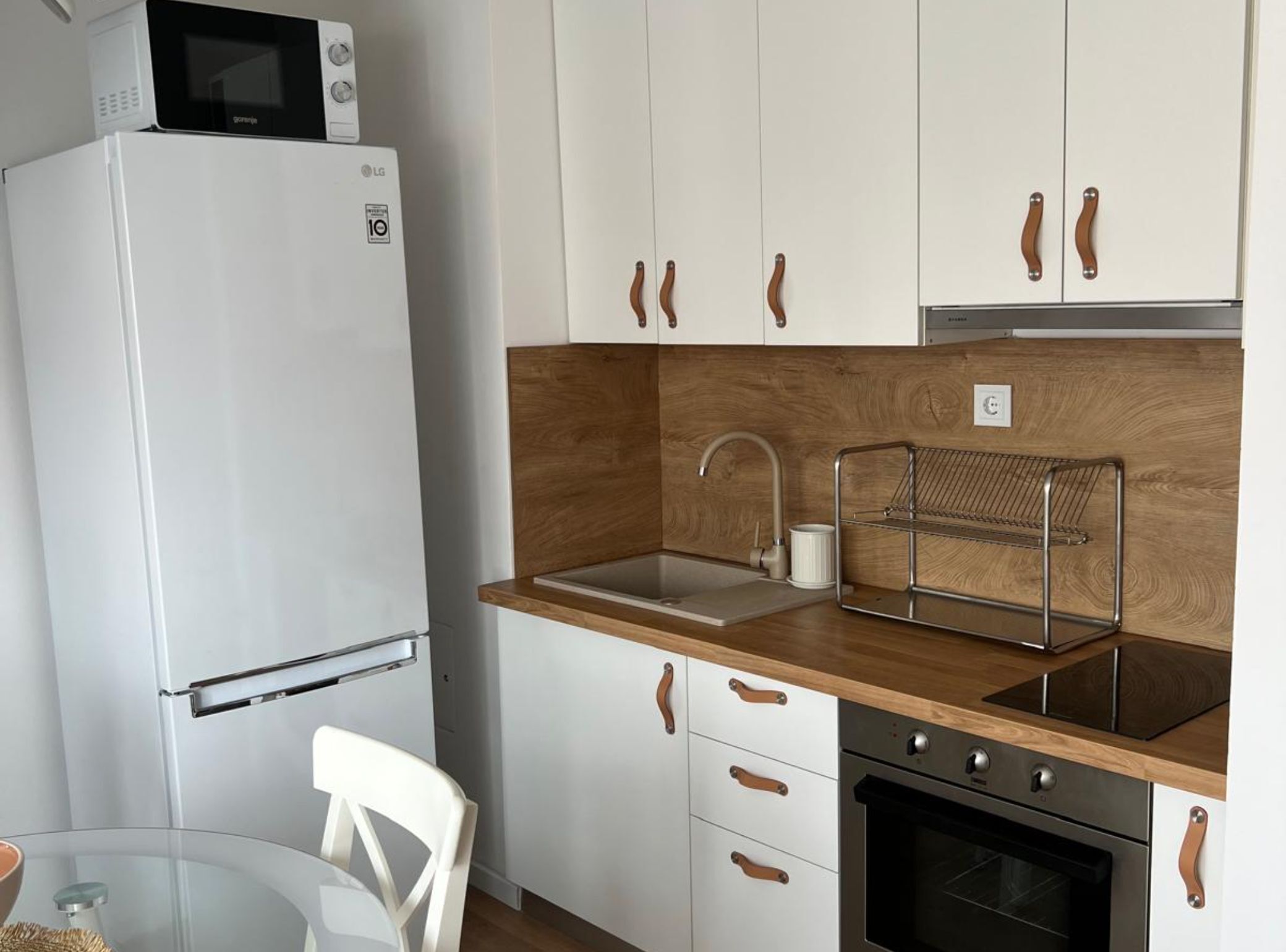 Eine kleine Küche mit weißen Schränken, einer Holz Arbeitsplatte, einer Edelstahl-Spüle, einer Mikrowelle und einem Backofen.