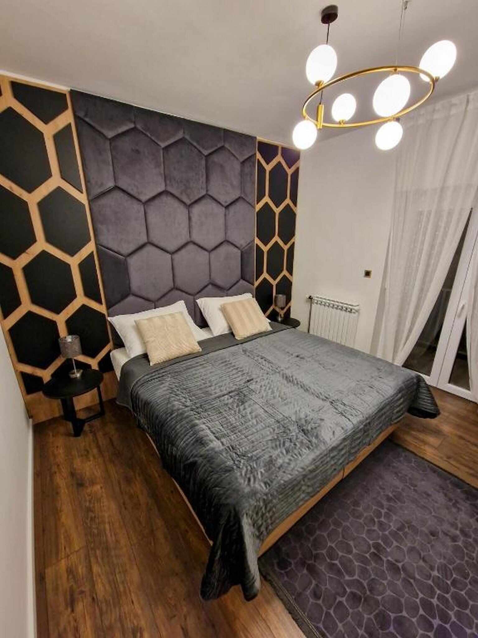 Ein modernes Schlafzimmer mit einem Kopfende mit geometrischem Muster, einer grauen gesteppten Bettdecke und einer runden Kronleuchter.