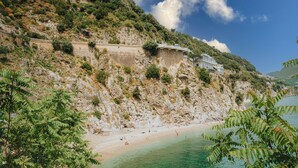 A coastal landscape with a rocky cliff, a beach, and a building on the cliff. - Villa San Michele by Elite Villas (Cetara)