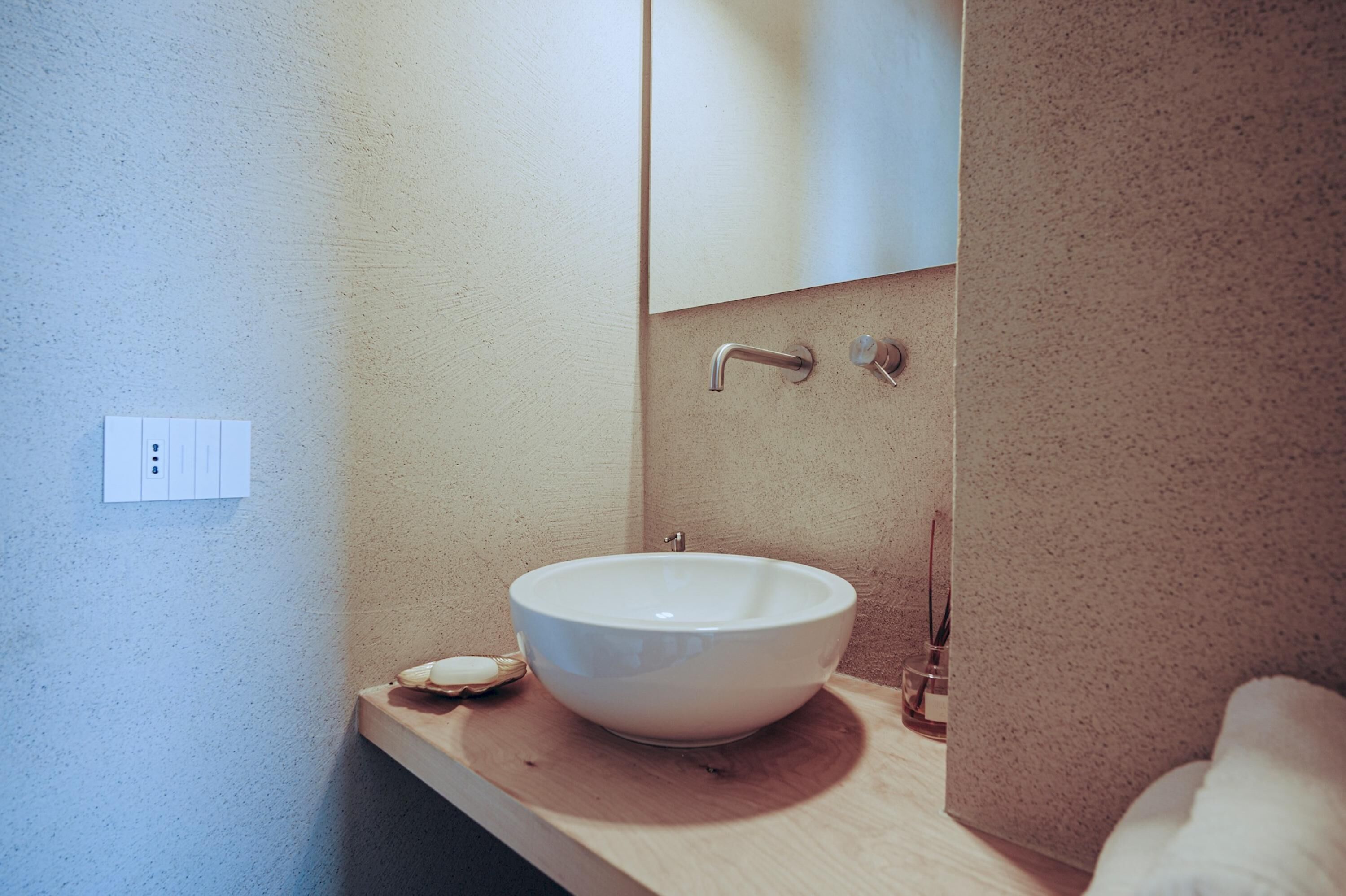 A modern bathroom with a white ceramic sink, a wooden countertop, a mirror, and a towel rack.