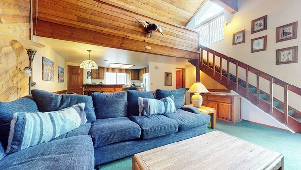 A cozy living room with a blue sofa, wooden ceiling, and a staircase leading to another level. - Large Rustic Home. Private Washer/Dryer, Centrally Located. Pool On-site (Mammoth Lakes)