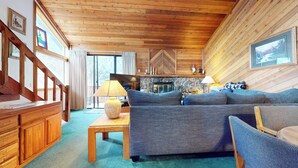 A cozy living room with a wooden ceiling, a stone fireplace, a sofa, and a television. - Large Rustic Home. Private Washer/Dryer, Centrally Located. Pool On-site (Mammoth Lakes)
