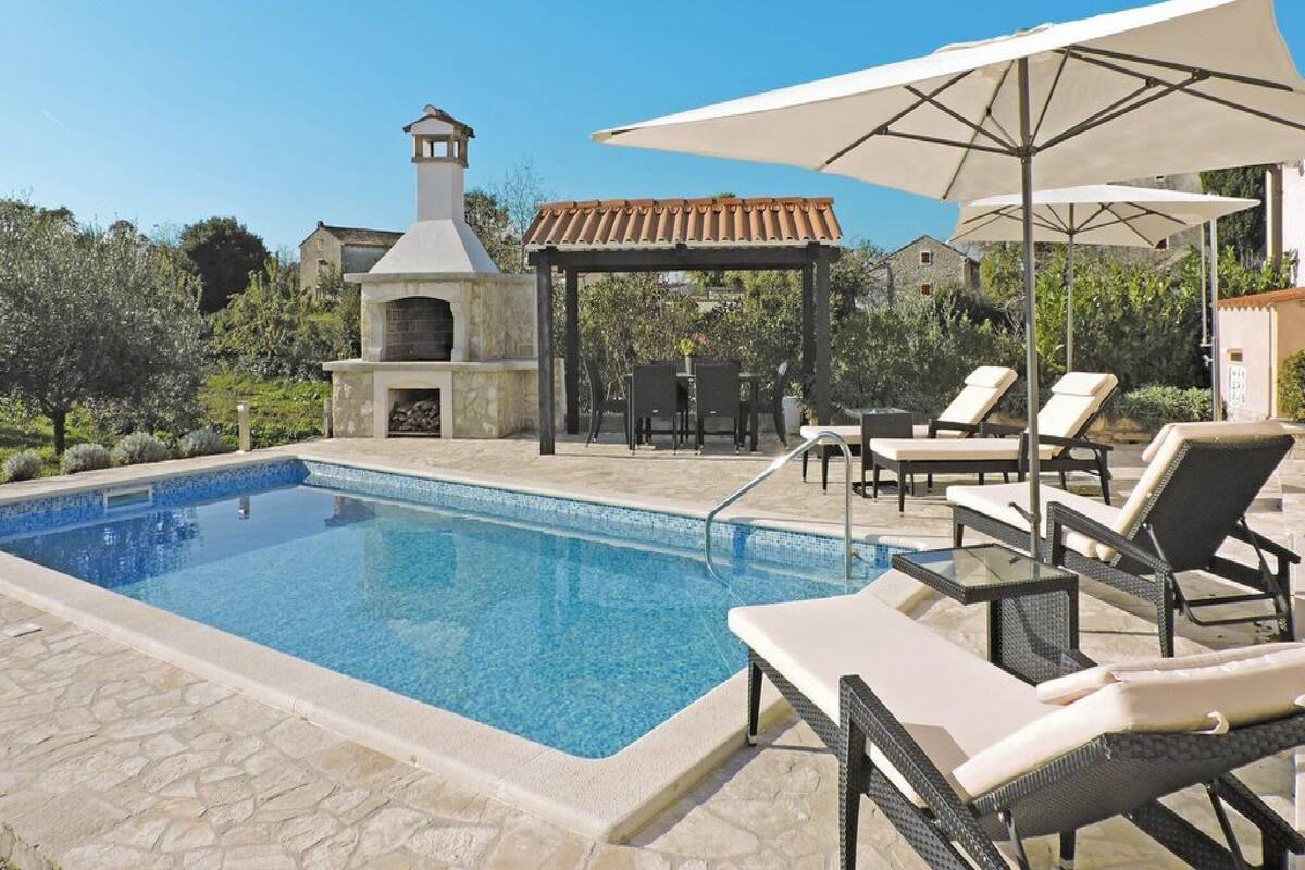 Une piscine avec des chaises longues et un espace barbecue.