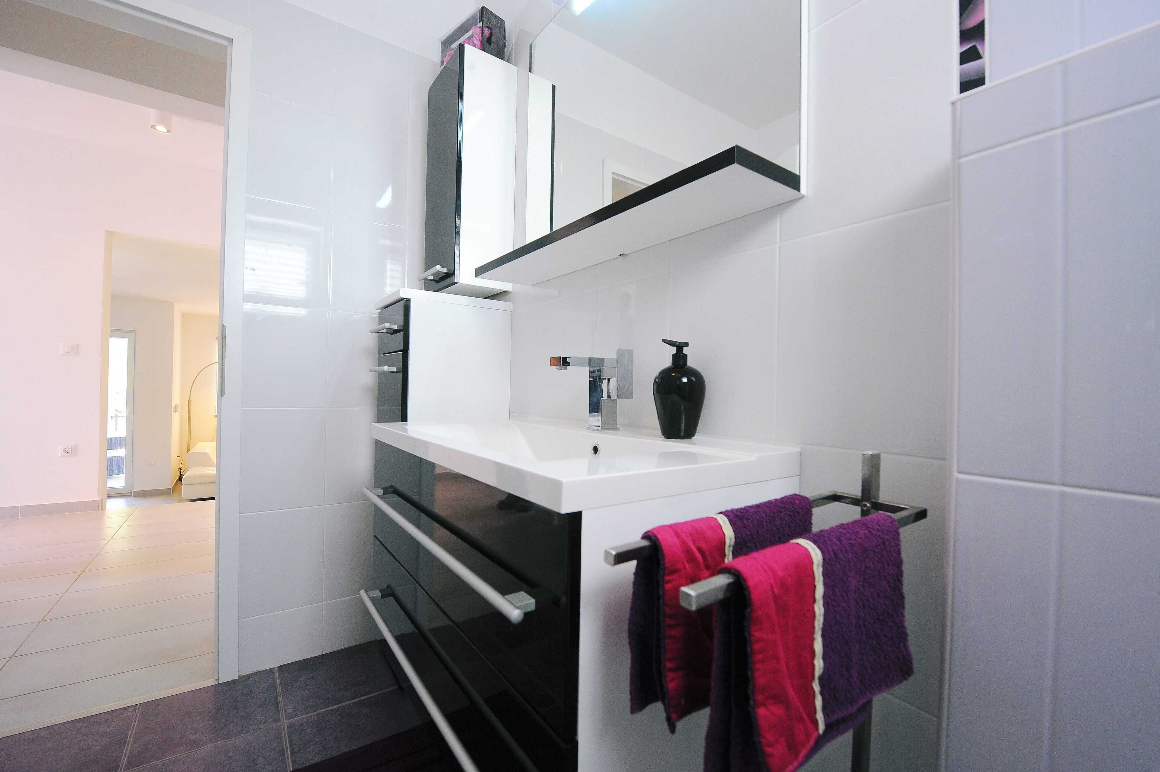 Un baño moderno con tocador blanco, un dosificador de jabón negro y dos toallas colgadas en un perchero.