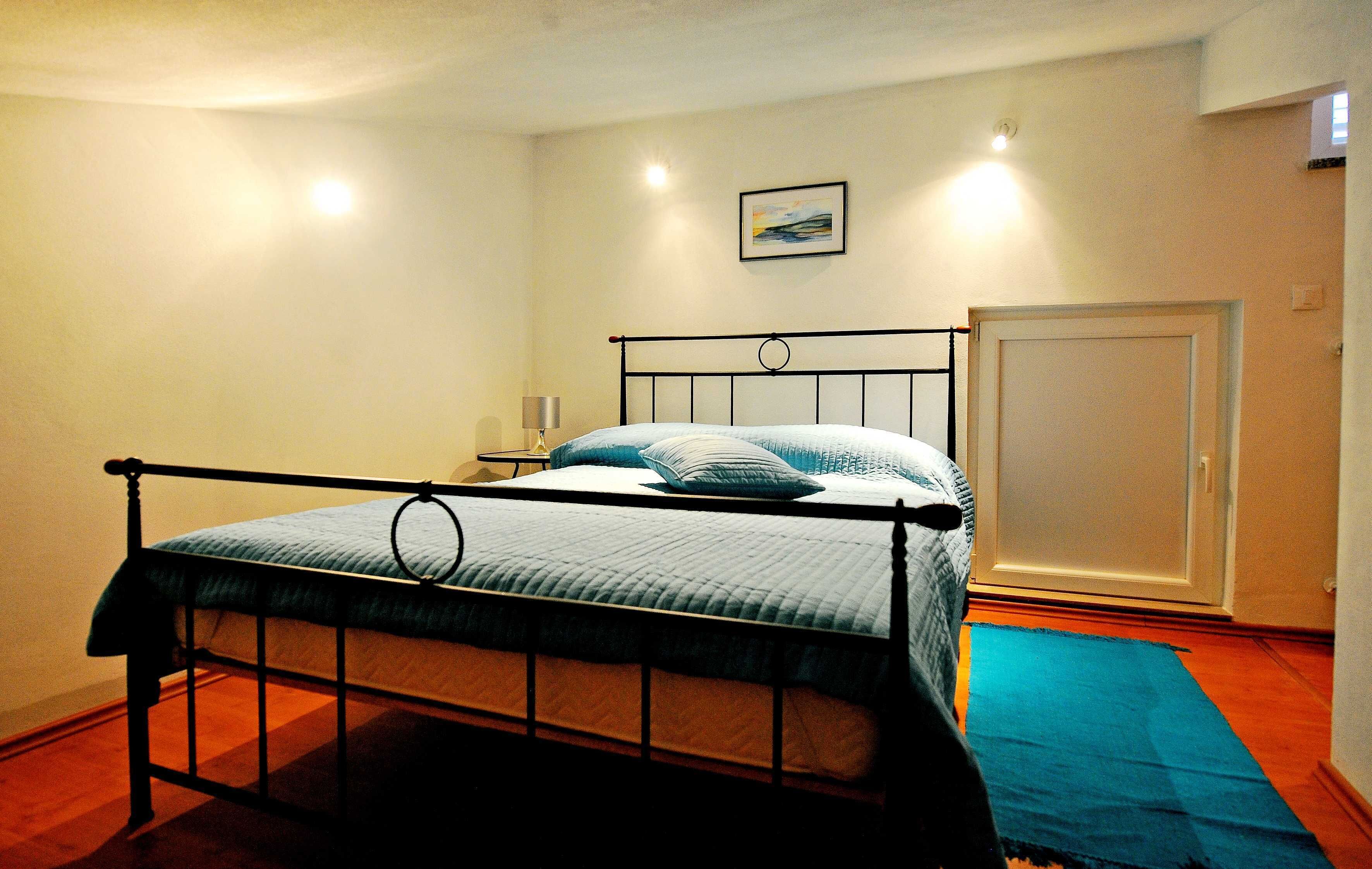 A single bed with a metal frame, a bedside table with a lamp, and a door to the right.
