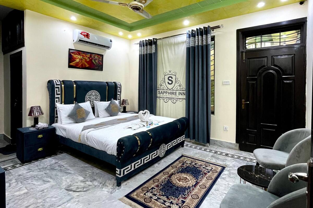 A hotel room with a bed, a desk, a chair, a ceiling fan, and a door.