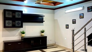 A spacious room with a modern ceiling design, a black entertainment unit, and a staircase. - Sapphire Inn (Islamabad)