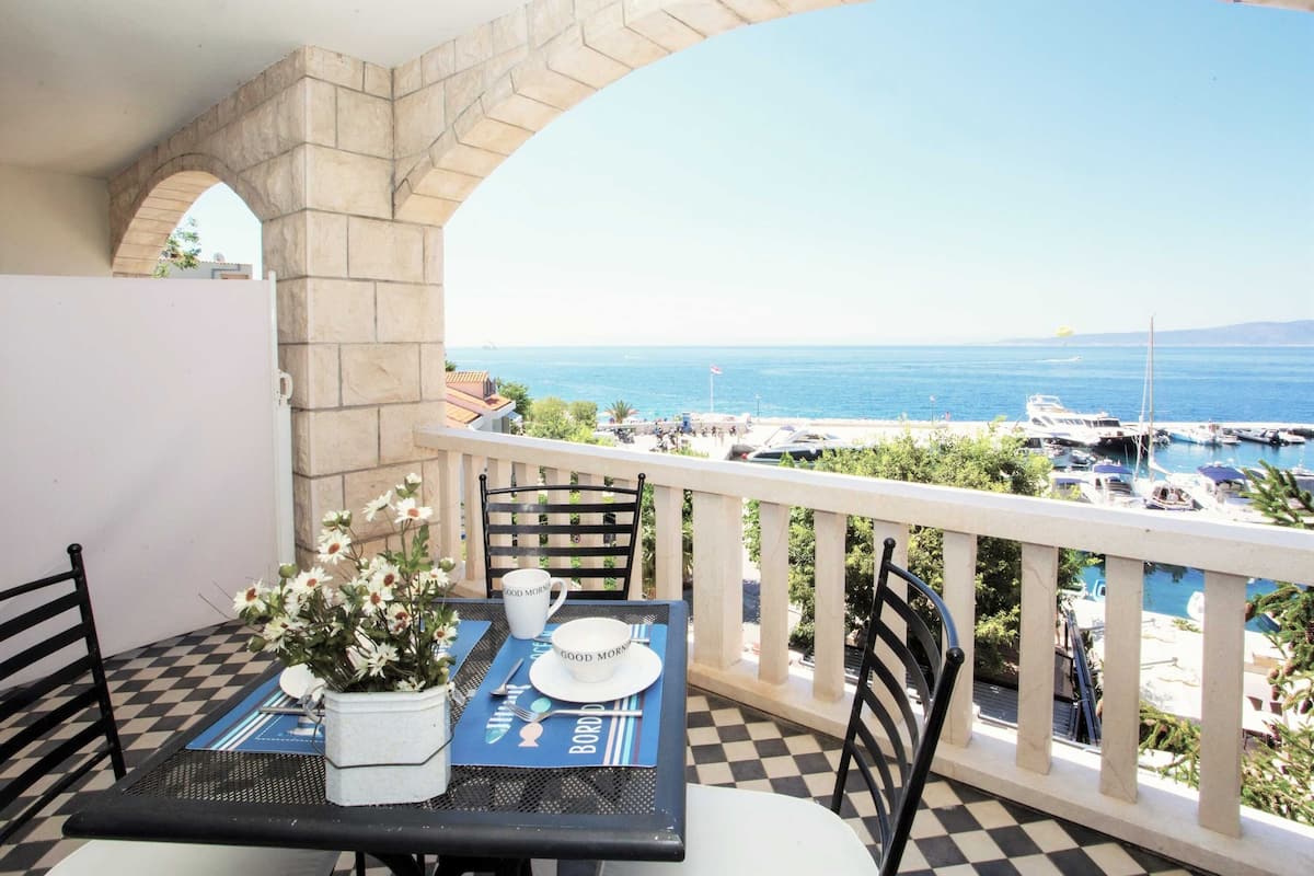 A balcony with a checkered floor, a table set with a flower vase, a cup, and a plate with "GOOD MORNING" text.