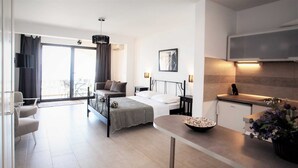 Una habitación de hotel moderna con cama, mesitas de noche, zona de comedor y cocina.
