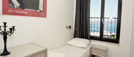 A bedroom with a bed, a nightstand, a dresser, a window with curtains, and a poster on the wall.