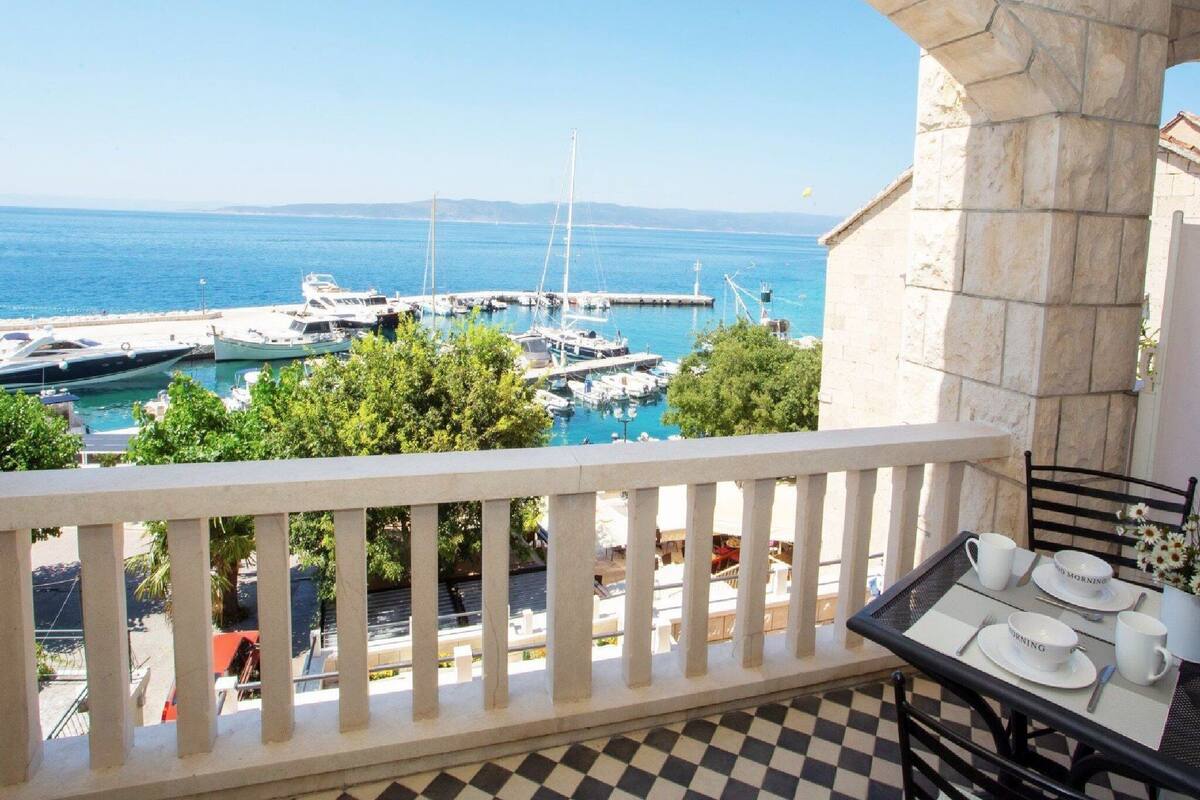 A balcony with a checkered floor, overlooking a marina with boats and a clear blue sea.