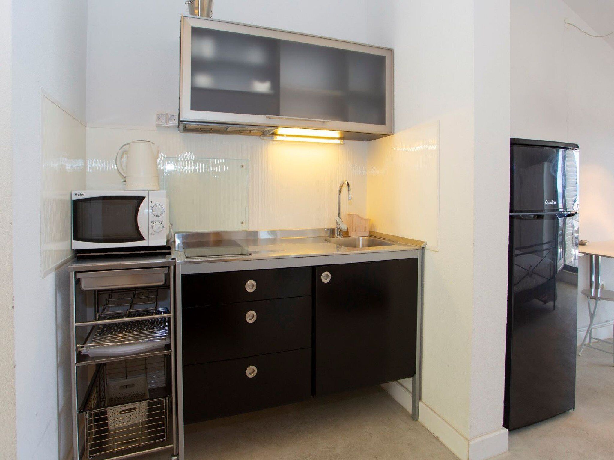 A compact kitchenette with a microwave, stove, sink, and black refrigerator.