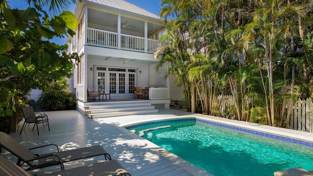 Ein zweistöckiges Haus mit Balkon, Schwimmbad und Palmen.