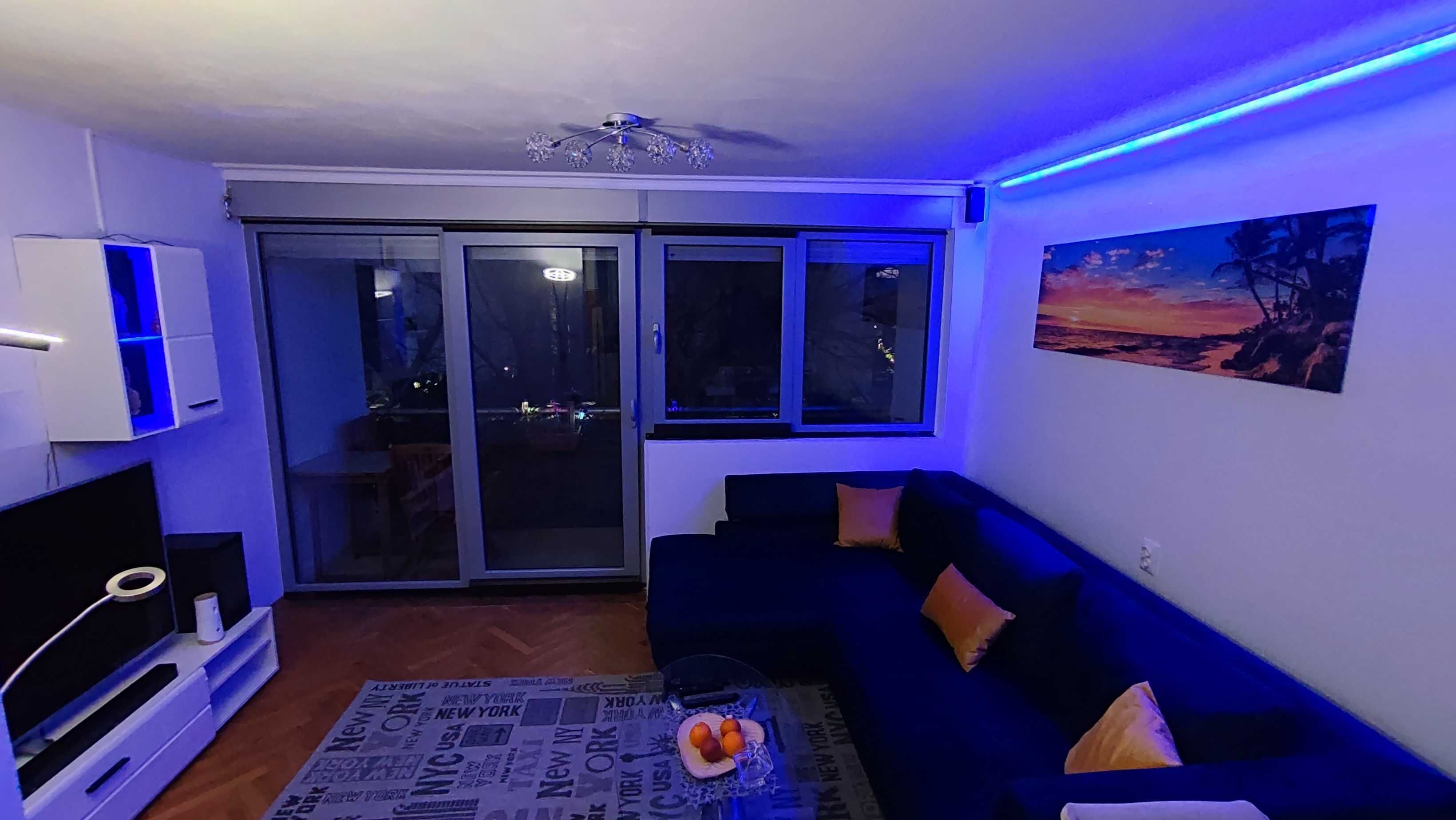 A living room with a dark blue sofa, a flat-screen TV, and a ceiling fan.