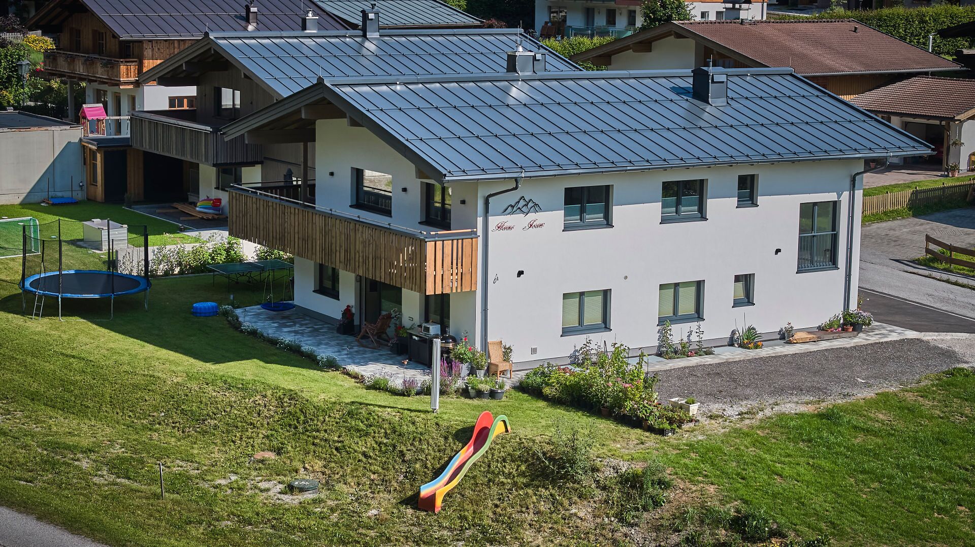 A modern two-story house with a metal roof, a trampoline, and a slide in the yard.