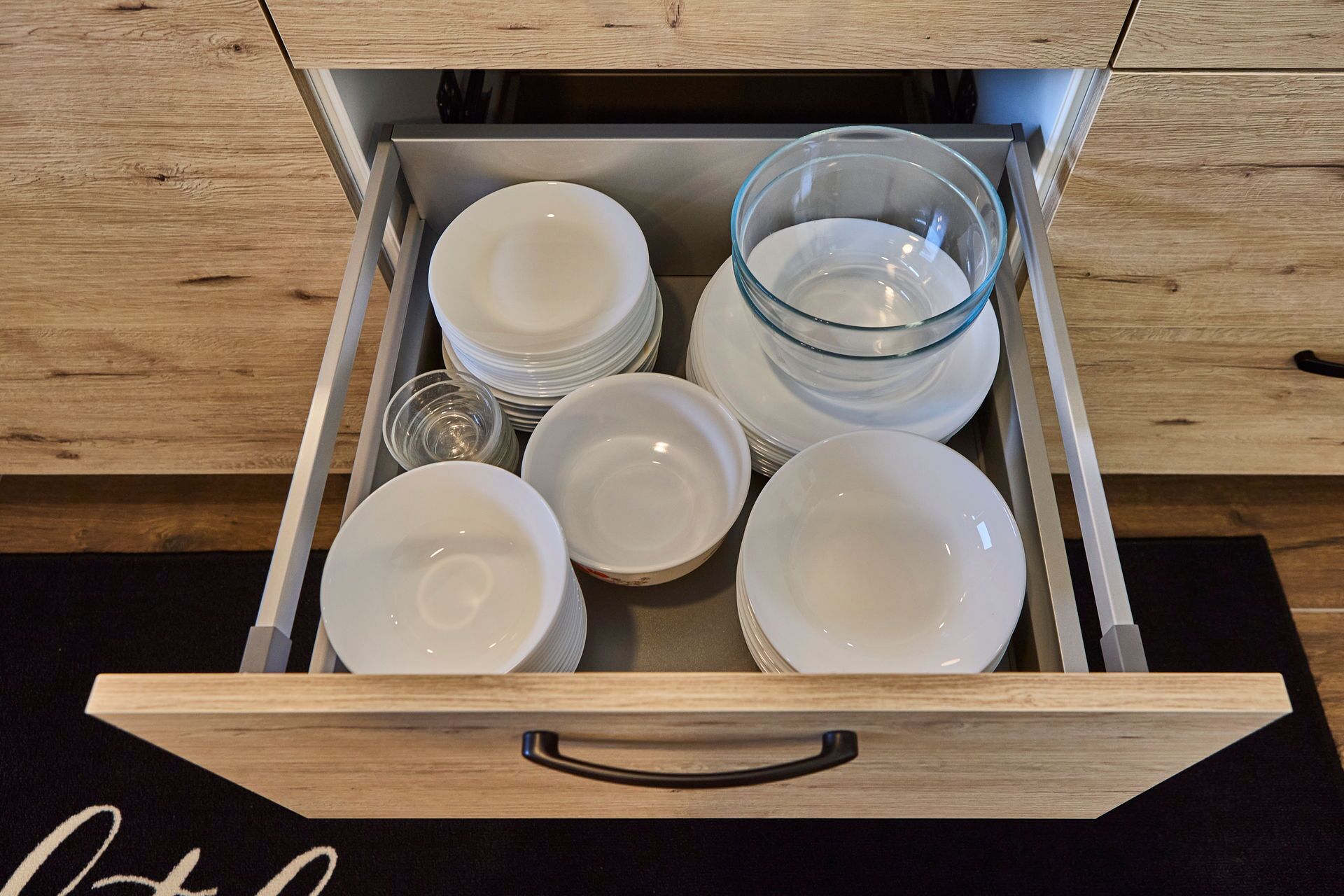 A drawer containing various white dishes and a clear glass bowl.