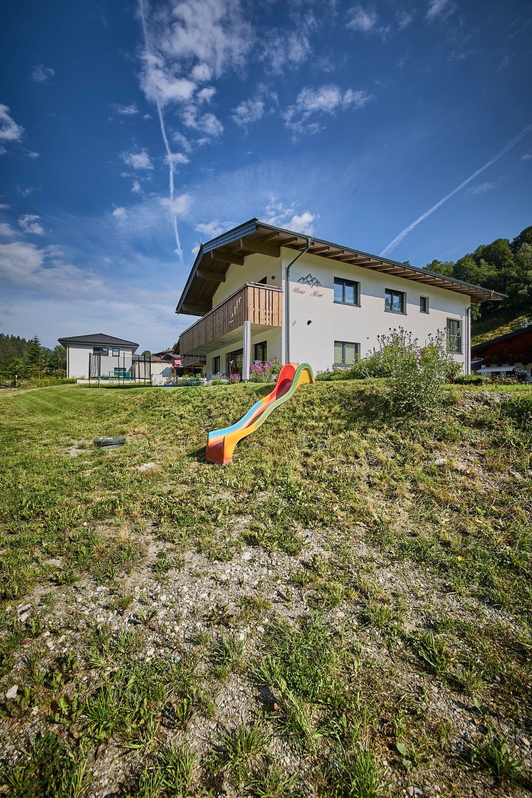 A modern two-story building with a balcony, a grassy area with a colorful slide, and a clear blue sky.