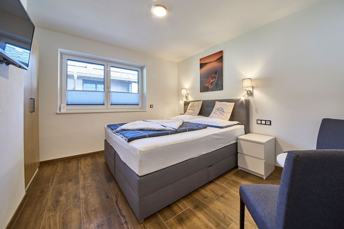Un dormitorio moderno con cama, mesitas de noche, una silla y ventana.