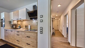 A modern kitchen with wooden cabinets, a built-in oven, and a microwave. - Haus Joan - Apartments (Saalbach-Hinterglemm)