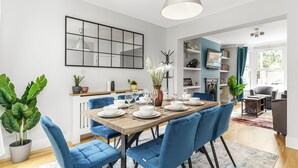 Ein moderner Essraum mit einem Holztisch, gedeckt für sechs Personen, blauen Polsterstühlen und einem großen Spiegel an der Wand.