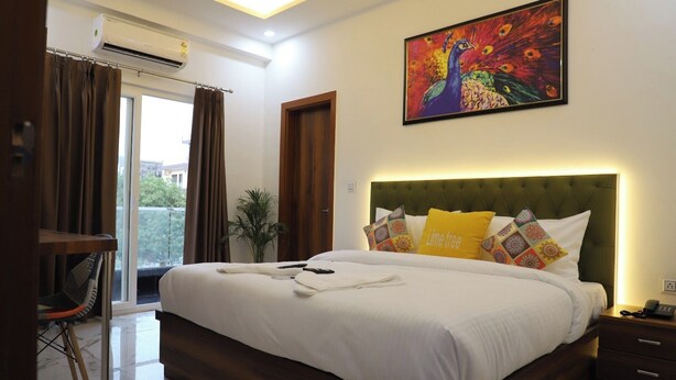 A hotel room with a large bed, a painting of a peacock, and a view of the outdoors. - Opulent Inn By Lime Tree Hotels (Greater Noida)