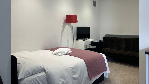 Una habitación de hotel con una cama, un escritorio con televisor, una lámpara roja y un sofá marrón.