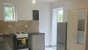 Una cocina compacta con estufa, horno y refrigerador. Hay una ventana con vistas a zonas verdes.