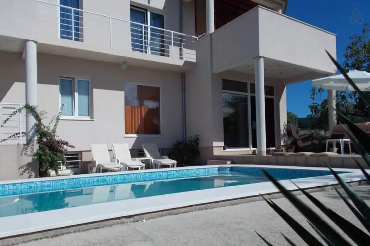 Un edificio moderno de dos pisos con piscina, sillas de descanso blancas y un patio cubierto.
